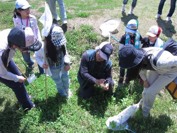 虫取り網を持った小学生と保護者が講師の大塚先生の授業を受けている写真